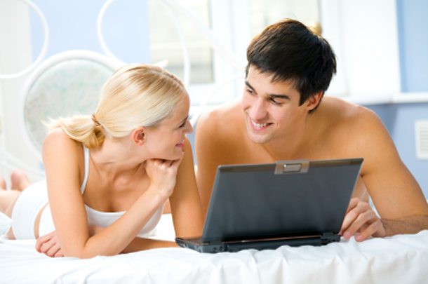 Couple looking for sex clubs on laptop in bed.